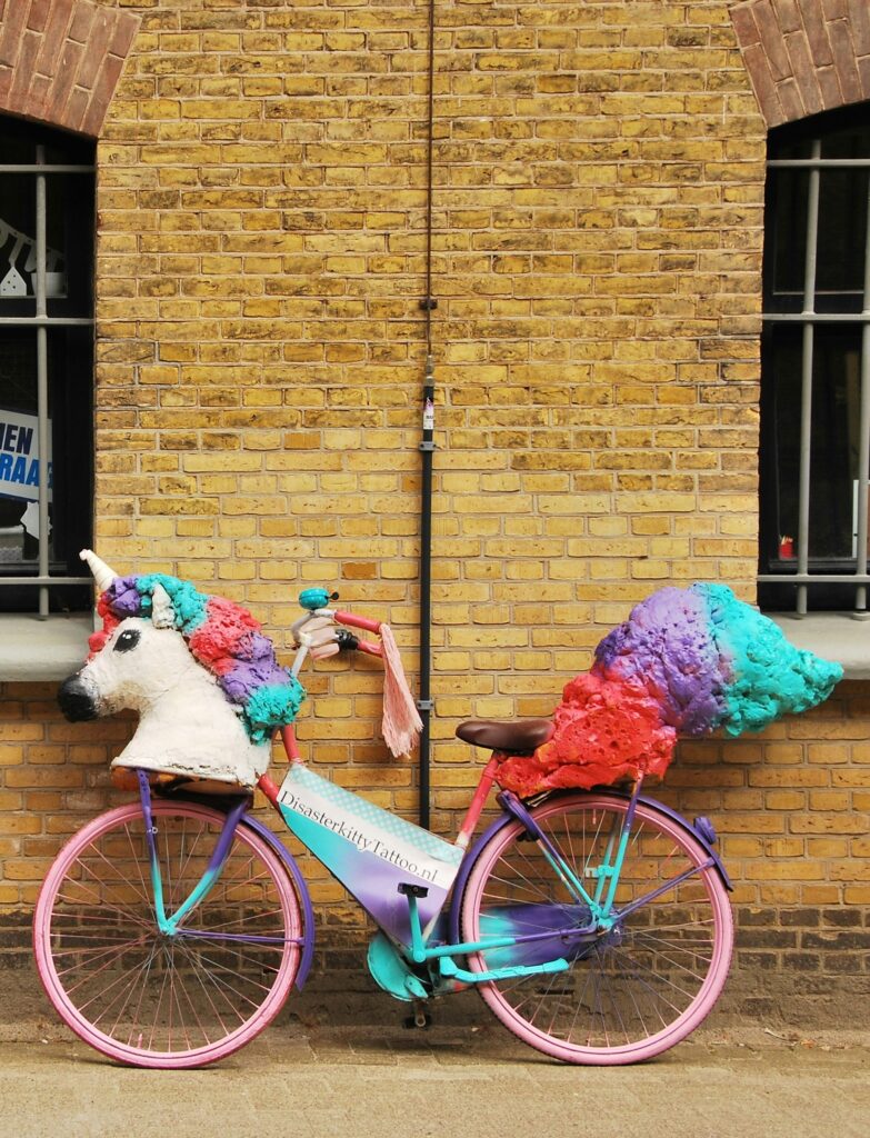 A bicycle with a unicorn puppet on handlebars leans against brick building